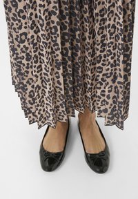 Faltiger, knielanger Rock in Beige mit schwarzem Leopardenmuster, kombiniert mit schwarzen Ballerinas aus Lackleder mit einer Schleifenakzent.