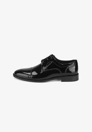 Chaussure habillée en cuir verni noir avec un bout arrondi, un laçage et des lignes épurées. Présente un petit talon empilé et des détails de couture discrets.