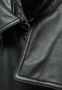 Col de veste en cuir noir avec couture détaillée et tirette de fermeture éclair argentée visible sur un fond sombre.