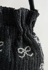 Melnā pērlīšu soma ar sakrautu augšdaļu. Rūpīgi izstrādāta virsma no mazām melnām pērlītēm un dekoratīvs sudraba raksts, kas atgādina lenti.