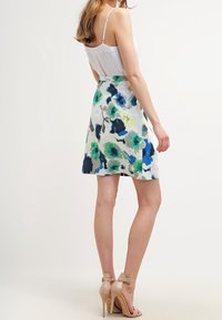 Květinová sukně v bílé barvě s modrými a zelenými vzory, krátká délka, lehká látka, doplněná béžovými sandály na vysokém podpatku.