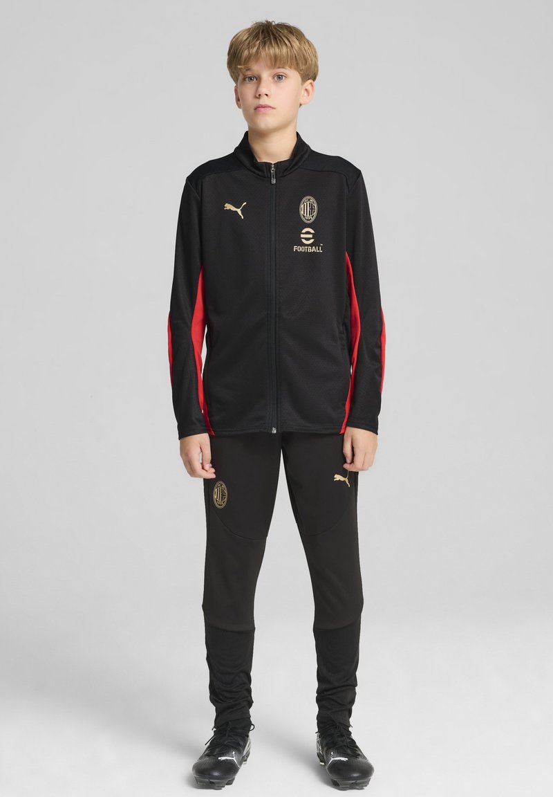 Zwarte sportieve trainingspak met gouden accenten, met een ritsjaket met rode mouwen en logo, gecombineerd met zwarte tapered broek.