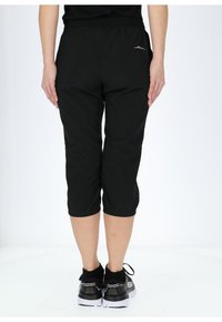 Pantaloni capri neri con vita elastica, caratterizzati da un orlo a risvolto e discreti dettagli di cucitura laterale, abbinati a scarpe sportive nere.