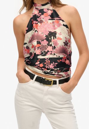 Ärmelloses Neckholder-Top mit hohem Kragen, schwarz-cremiger Basis, pinkem Blumen- und Lotusmuster, kombiniert mit weißen Hosen und schwarzem Gürtel mit goldener Schnalle.