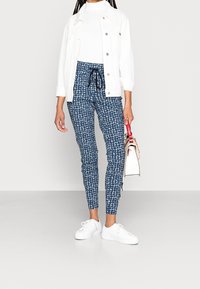 White denim jacket over a white top, paired with navy patterned skinny pants featuring a drawstring waist. White sneakers and small handbag.