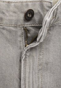 Primer plano de tela de mezclilla gris, con un zipper visible, un botón de metal y un detalle de costura prominente a lo largo del borde.