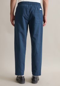 Marineblauwe broek met elastische tailleband en rechte pijpen, voorzien van een achterzak en een gladde, textuurstof.