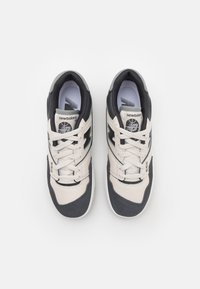 Paire de baskets New Balance 550 noir et blanc avec lacets noués, vues de dessus sur un fond blanc uni.