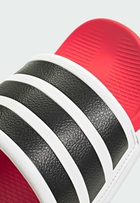 Sort slidesandal med tre hvide teksturerede striber, med en rød polstret indersål og gummisål med et ribbet mønster.