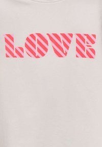 T-shirt gris clair arborant un texte en rose vif qui dit "AMOUR" avec un motif de rayures diagonales sur les lettres. Texture lisse.