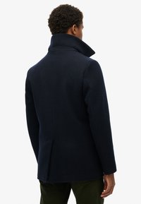 Marineblå uldfrakke med høj krave, skræddersyet pasform og enkelt slids bagpå. Har en glat tekstur og rene linjer.