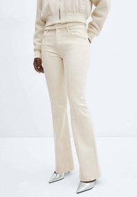 Pantalon beige évasé en denim doux, doté de poches avant et de coutures décoratives, assorti à des escarpins argentés brillants à bouts pointus.