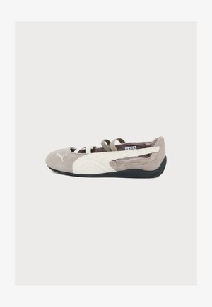 Baskets légères marron clair et blanches sans lacets avec des brides élastiques et une semelle noire texturée, vues de profil sur un fond blanc uni.