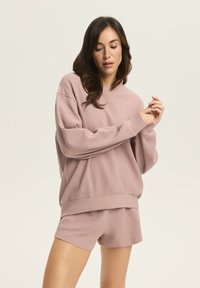 Świeży sweter z dżerseju w kolorze jasnego malwy i pasujące szorty, z luźnym krojem i ribbowanym dołem. Miękki i wygodny materiał.