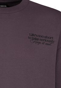 Lila Sweatshirt aus weichem Stoff mit Rundhalsausschnitt und bedrucktem Text auf der linken oberen Seite: "Das Leben ist zu kurz, um es ernst zu nehmen. Bleib cool."