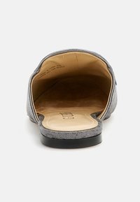 Pantofii slip-on din material gri au o branț neted de culoare bej, un design cu spatele deschis, un toc mic negru și detalii de cusătură de-a lungul marginilor.