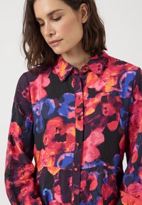 Colorful button-up shirt featuring a floral pattern in shades of red, pink, blue, and orange against a black background. Soft, textured fabric.