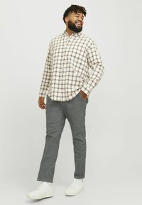 Rutig skjorta i beige och brunt, kombinerad med grå byxor och vita sneakers. Skjortan har en avslappnad passform och långa ärmar.