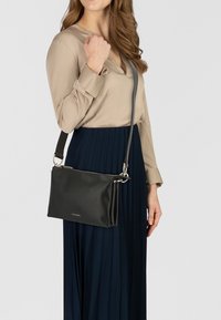 Borsa a tracolla in pelle nera con ferrature argentate, chiusura lampo e dettaglio logo. Dotata di una lunga tracolla regolabile e di una forma rettangolare elegante.