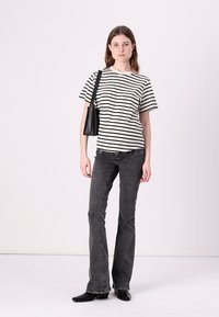 Tricou în dungi alb-negru, cu mâneci scurte. Blugi negri cu talie înaltă, cu croi evazat, dintr-un material texturat. Accesoriile includ o geantă mică neagră.
