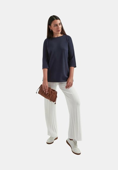 Top a maniche lunghe navy, pantaloni bianchi plissettati e sneakers bianchi. Borsa marrone con design arricciato. Insieme di abbigliamento semplice e moderno.