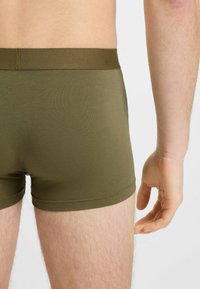 Boxer shorts verde oliva con una texture liscia, elastico in vita e design a gamba corta. Vista da dietro, che mostra una copertura minima.
