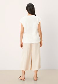 Bílý krátký rukáv top s volným střihem, spárovaný s širokými kalhotami v světlé béžové barvě. Hladká textilie, minimalistický design a neutrální barvy.