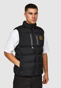 Zwarte gewatteerde vest met een hoge kraag, ritssluiting en voorzakken. Bevat een ronde patch op de linkerborst en accentuerende details in het wit.