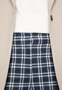 Beige blazer över en vit topp, kombinerad med marinblå rutiga byxor med blå och vita rutor och subtil textur.