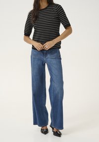 Sort-hvid stribet kortærmet top parret med brede blå jeans og sorte højhælede sko, med en afslappet pasform og denimtekstur.