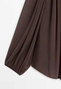 Manche longue d'un chemisier marron avec poignet élastique froncé et texture de tissu douce.