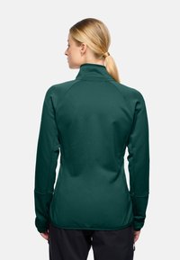 Top atletico verde a maniche lunghe con colletto alto, tessuto testurizzato e maniche raglan. Presenta fori per il pollice ai polsini e un design aderente.