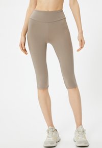 Leggings capri beiges hechos de un tejido elástico con una cinturilla alta y una textura suave, que terminan justo debajo de la rodilla.