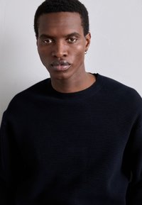 Dunkelblauer gerippter Pullover mit rundem Ausschnitt und langen Ärmeln, der aus einem strukturierten Stoff gefertigt ist. Einfaches Design ohne zusätzliche Muster.
