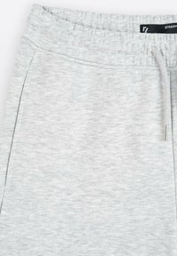 Jasnoszare dresy z teksturowanej tkaniny, z elastycznym pasem i sznurkiem do regulacji. Posiada boczne kieszenie dla wygody.