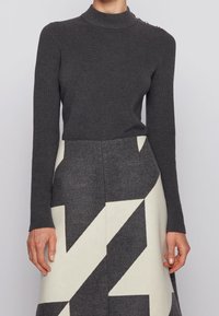 Pull à col roulé côtelé gris foncé à manches longues, associé à une jupe longueur genou ornée de motifs géométriques audacieux en gris et blanc cassé.