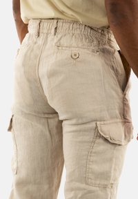Beige cargobroek met een elastische tailleband, zijzakken en een achterzak met een knoopsluiting. Gestructureerde stof met een relaxte pasvorm.