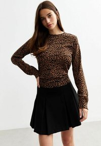 Haut à manches longues en imprimé léopard brun et noir, associé à une mini-jupe plissée noire. Tissu doux, taille ajustée et col rond.