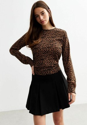 Top de manga larga con estampado de leopardo en marrón y negro, combinado con una falda corta plisada negra. Tejido suave, cintura ajustada y escote redondo.