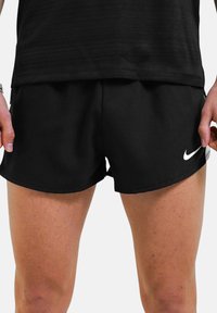Pantaloni sportivi neri realizzati in materiale leggero, con un orlo curvo e il logo Nike bianco di lato.