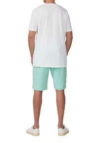 Witte katoenen t-shirt met korte mouwen, gecombineerd met mintgroene shorts. Witte schoenen maken de casual outfit compleet.
