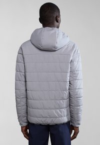 Chaqueta acolchada de un gris claro con capucha, patrón de acolchado horizontal y puños elásticos. La vista trasera muestra una textura suave y un diseño limpio.