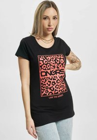 Melna T-krekls ar īsām piedurknēm, kuram ir drosmīgs sarkans leoparda raksta grafikas attēls un uzraksti "DNGRS" un "LOVE THE DANGER" zem tā.