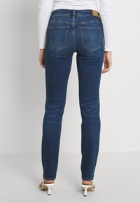 Dünne Jeans aus dunkelblauem Denim, mit einer mittelhohen Taille, Gesäßtaschen mit Nähdetails und einer schmalen Passform entlang der Beine.
