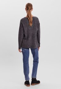 Maglione grigio lavorato a maglia con vestibilità ampia, scollo rotondo e texture a coste, abbinato a jeans di denim blu e stivaletti neri alla caviglia.