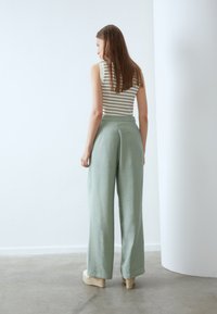 Stribet ærmeløs top og lysegrønne brede bukser med en glat tekstur. Sat mod en minimalistisk baggrund.