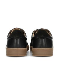 Zapatillas de cuero negro con textura suave, suelas de goma marrón y forma redondeada. Cuentan con un talón acolchado y detalles de costura sutiles.