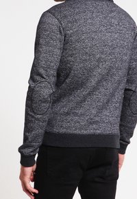 Sudadera gris texturizada con escote redondeado, puños acanalados y parches en los codos, que presenta un diseño entallado y una tela suave.