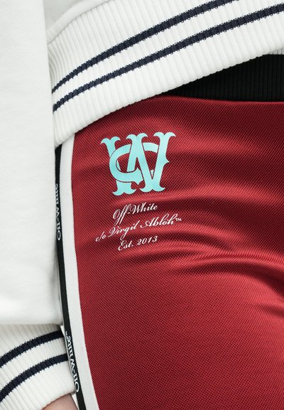 Raudoni audiniai šortai su tinklo tekstūra, akvamarino spalvos logotipo dizainu ir baltu tekstu, rašančiu "Off White" su "Established 2013" kursyvu.