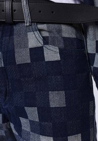 Pantalones de cuadros azul oscuro hechos de denim con tejido texturizado, que cuentan con un cinturón negro en la cintura y un bolsillo frontal.
